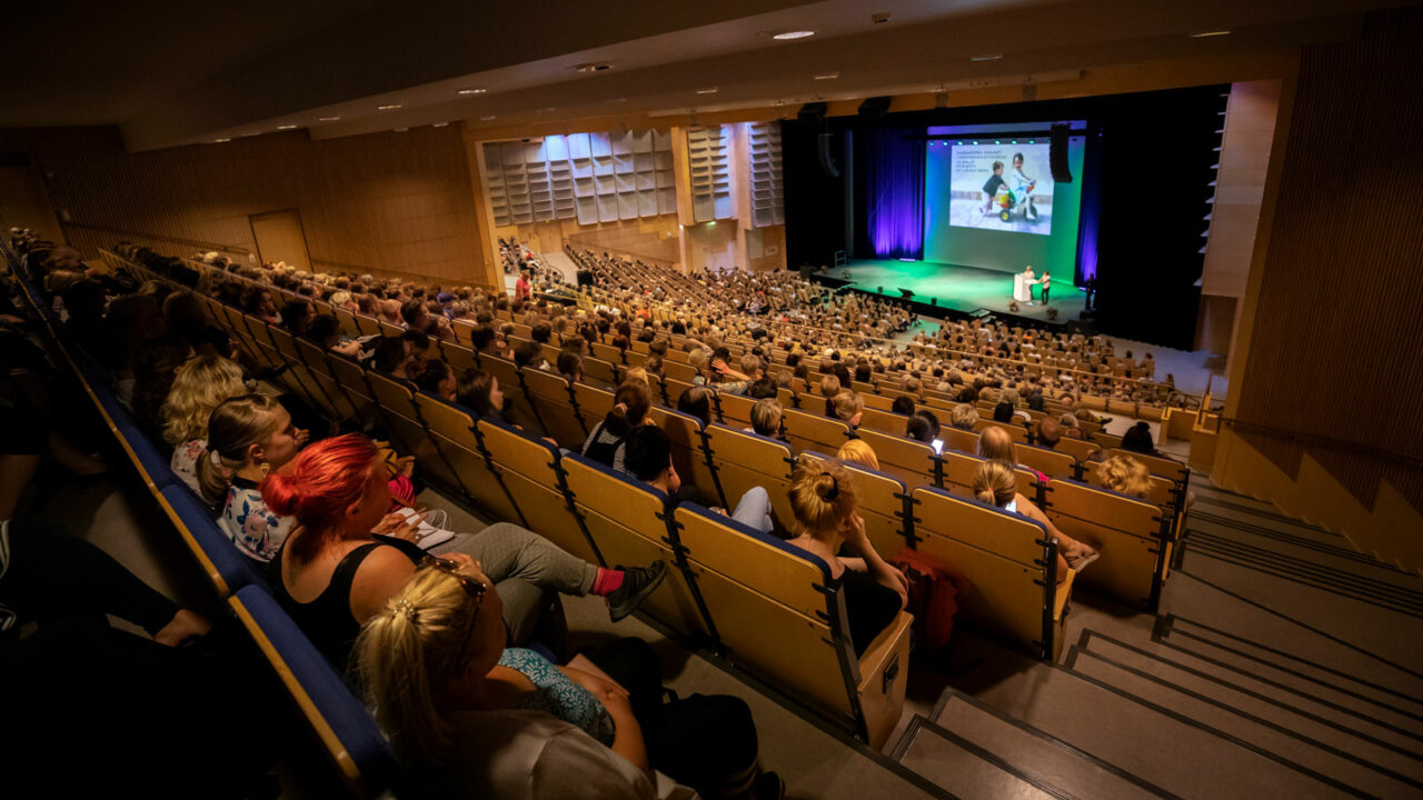 Henkilöitä istumassa Paviljongin kongressisalissa.